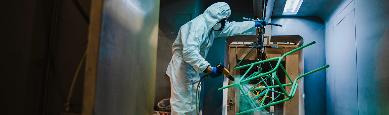 Mitarbeiter trägt Schutzkleidung und trägt Pulverbeschichtung mit Sprühpistole auf eine Metallkonstruktion auf.
