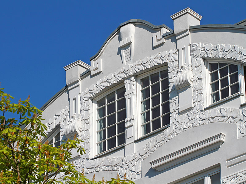 frisch renovierte weiße Außenfassade an einem Wohnhaus am Bodensee mit Rundgiebel und Stuckornamenten